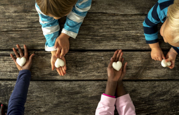 Barn som sitter vid ett träbord och håller fram vita stenhjärtan i händerna