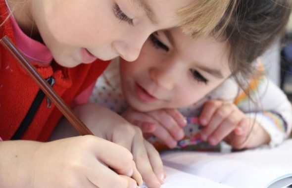 Två skolbarn som koncentrerat skriver och tittar på någonting i en skrivbok