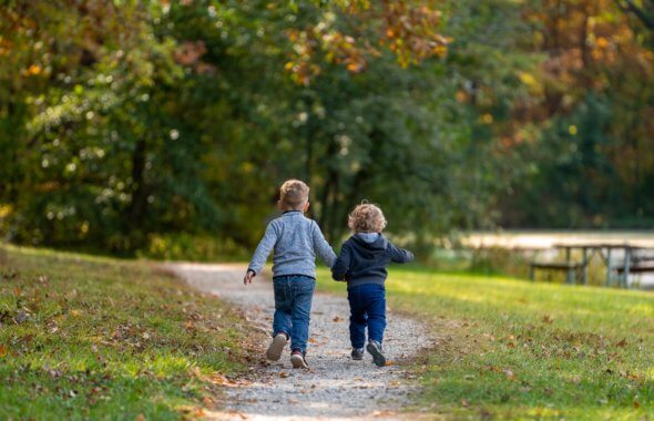 två pojkar som går hand i hand på en stig mot skogen