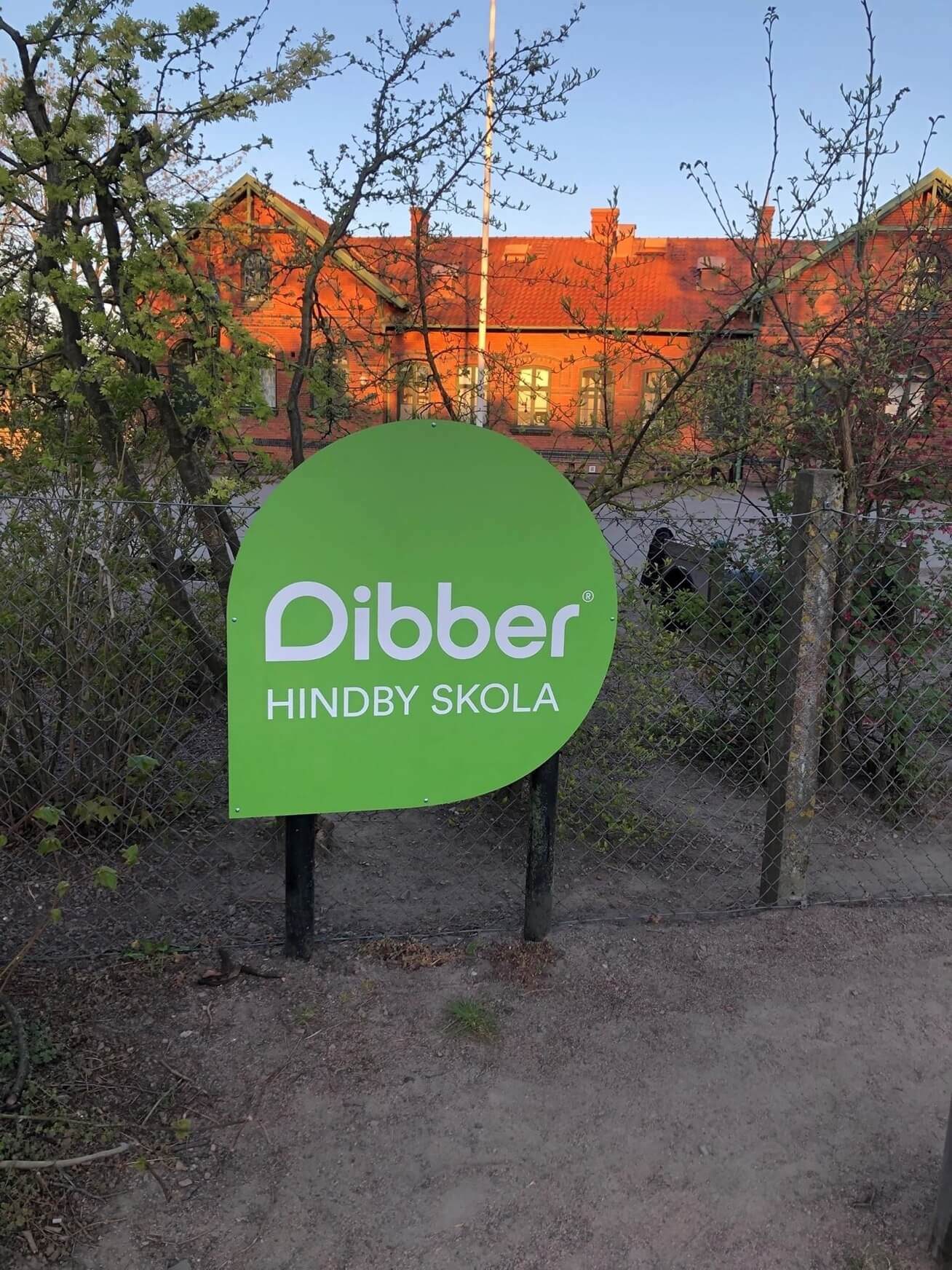 Hindby Dibber skola med loggan på staketet i fokus och själva skolan i bakgrunden